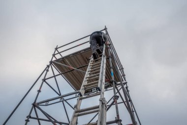 Adam uzatma merdiveniyle iskeleye tırmanıyor.