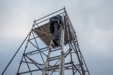 Adam uzatma merdiveniyle iskeleye tırmanıyor.