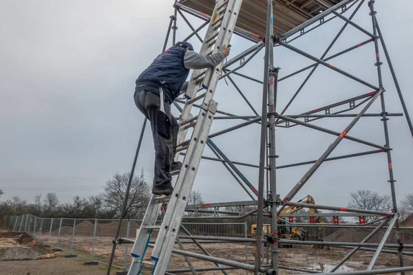 man climbs onto scaffolding on an extension ladder