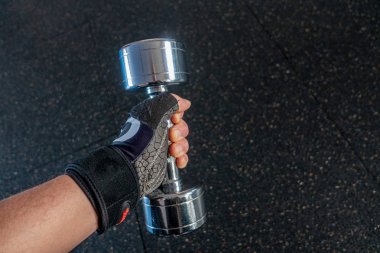 Spor salonunda eldivenli bir el gümüş bir dambıl tutar.