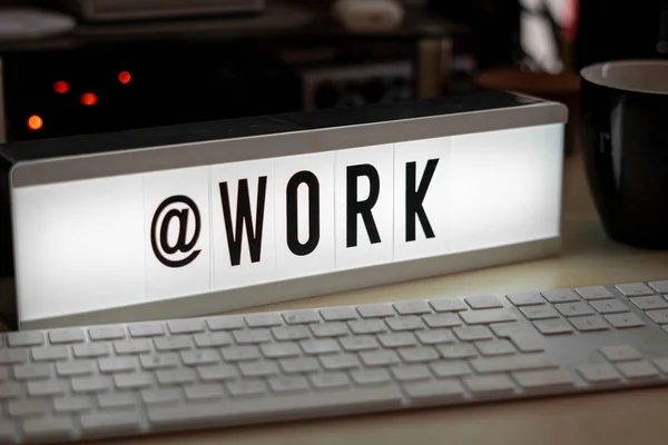 a white illuminated cinema sign with black letters @WORK