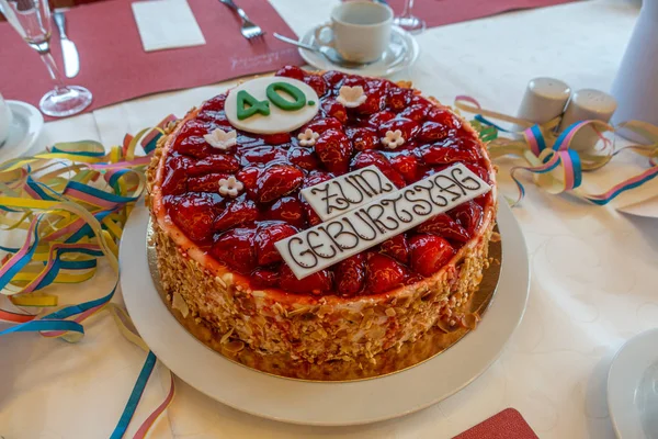 on a table with a white tablecloth there is a red birthday strawberry cake with the inscription \