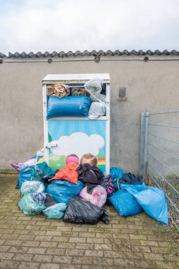 Yanı başında giysi dolu çöp torbaları olan aşırı dolu bir konteynır.
