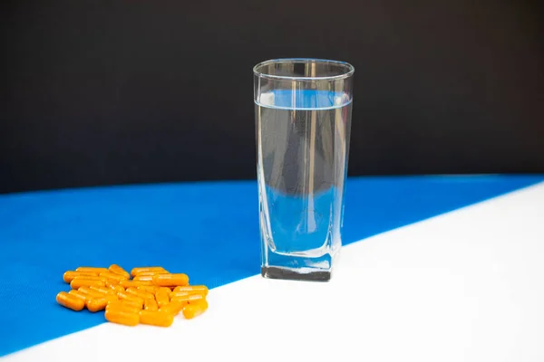 Ένα Ποτήρι Νερό Στέκεται Δίπλα Πολλά Πορτοκαλί Χάπια Λευκό Μπλε — Φωτογραφία Αρχείου