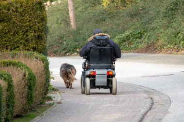 an old man drives an electric wheelchair and is accompanied by his faithful dog clipart