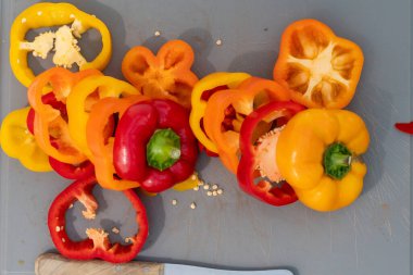 Kesme tahtasının üzerinde üç dilimlenmiş biber ve bir bıçak var.