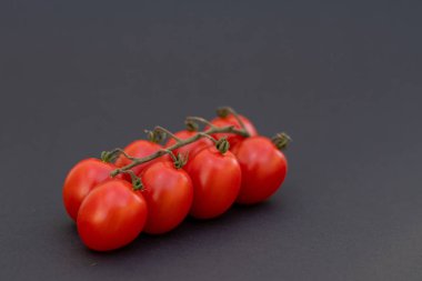 Karanlık bir üste, üzerinde sekiz küçük domates olan bir domates dalı.
