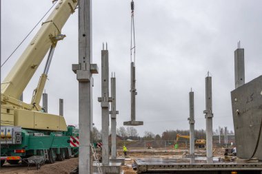 Büyük bir inşaat sahasına birçok beton kolon bir vinç yardımıyla yerleştirilir.