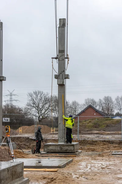 Sarı yağmurluklu bir inşaat işçisi büyük bir beton sütunun ereksiyonunu denetliyor ve kontrol ediyor.