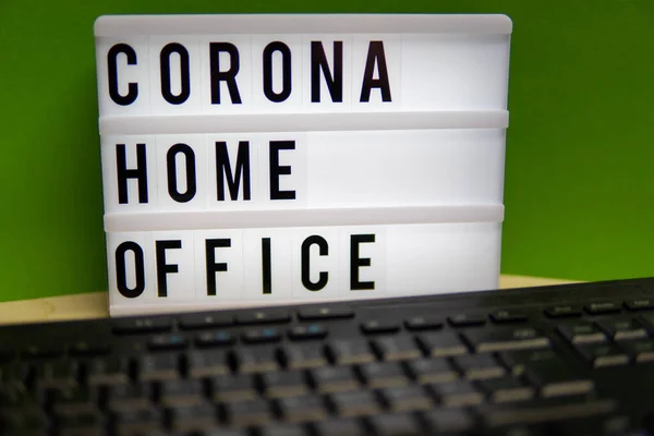 a light box with the inscription Corona Home Office stands on a desk and in front of it is a keyboard