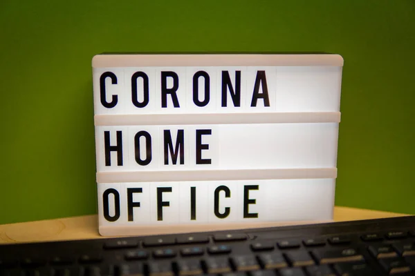 a light box with the inscription Corona Home Office stands on a desk and in front of it is a keyboard