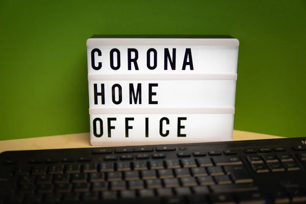 a light box with the inscription Corona Home Office stands on a desk and in front of it is a keyboard