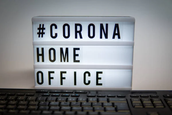 a light box with the inscription: #CORONA HOME OFFICE is behind a black computer keyboard against a gray background