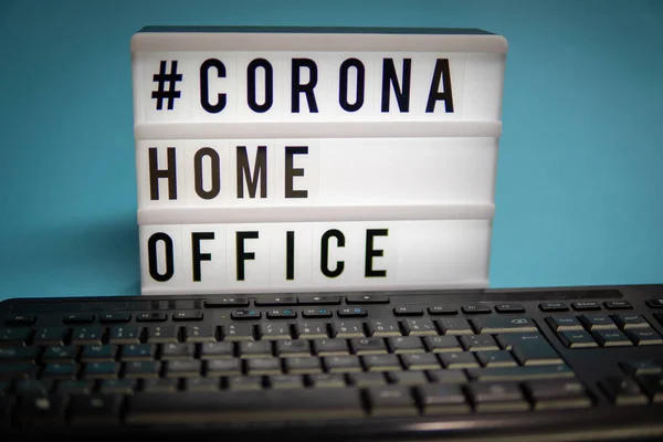 a light box with the inscription: #CORONA HOME OFFICE is behind a black computer keyboard against a blue background