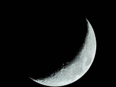 Ay kraterleriyle yükselen orak şekilli çeyrek ay kara gece gökyüzünde duruyor.