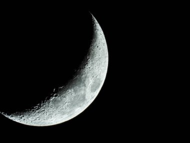 Ay kraterleriyle yükselen orak şekilli çeyrek ay kara gece gökyüzünde duruyor.