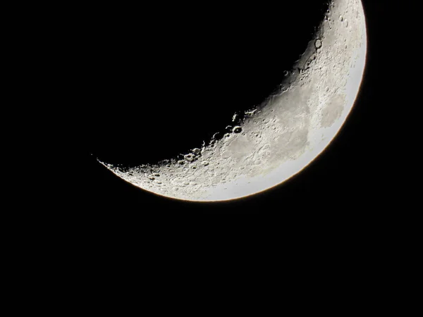 the increasing sickle-shaped quarter moon with its moon craters stands in the black night sky