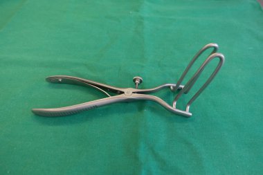 Cerrahi anal genişletici, yeşil bir cerrahi perdenin üzerinde yatıyor.