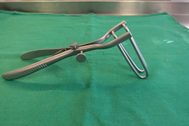 Cerrahi anal genişletici, yeşil bir cerrahi perdenin üzerinde yatıyor.