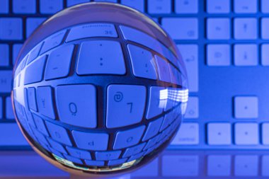 Bir kristal berrak cam top beyaz bir bilgisayar klavyesinin önünde duruyor ve biz renkli bir şekilde aydınlanıyoruz.