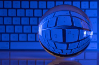 Bir kristal berrak cam top beyaz bir bilgisayar klavyesinin önünde duruyor ve biz renkli bir şekilde aydınlanıyoruz.