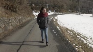 Karlı bir dağ manzarasında yolda yürüyen bir kız.