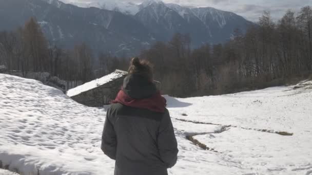 Sobre el hombro disparo de una chica con vistas a una cabaña en la nieve — Vídeos de Stock