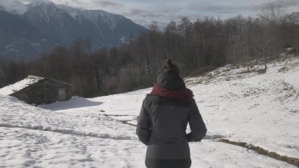 Sledování záběr dívky kráčející na sněhovém poli v blízkosti horské kabiny — Stock video