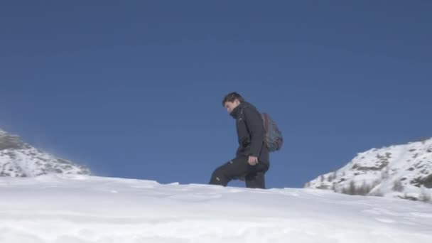 Draaiend schot van een wandelaar die de top van een besneeuwde winderige piek bereikt — Stockvideo