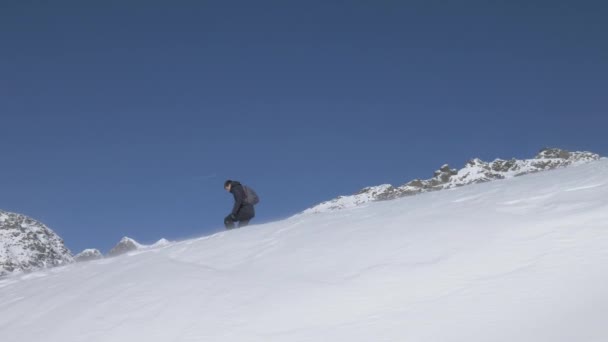 Tracking shot of a hiker descending a snow ridge in the mountains — 비디오