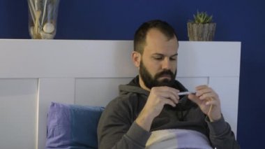 Coronavirus 'lu bir adam ateşini okuyor ve burnunu siliyor.