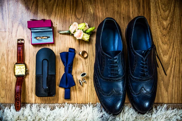 Wedding groom accessories : black shoes, wrist watch, perfume bottle, bow tie near wedding rings.details of the wedding morning of the bride\'s shoes, strap, butterfly, watches