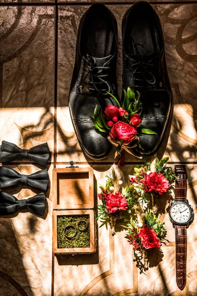 Wedding groom accessories : black shoes, wrist watch, perfume bottle, bow tie near wedding rings.details of the wedding morning of the bride\'s shoes, strap, butterfly, watches