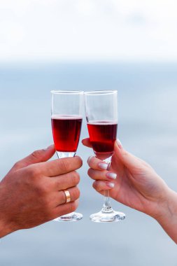 Ellerinde kırmızı şarap olan kadehler denizin arka planında.