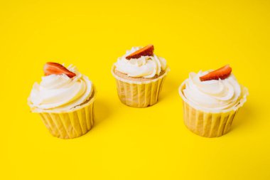 Sarı arka planda beyaz kremalı ve çilekli kekler. Pişirme ve tatlılar.