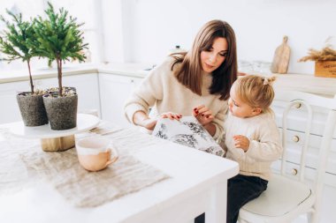 Anne kızını kaşıkla besler. Aile aydınlık mutfakta.. 