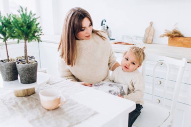 Anne kızını kaşıkla besler. Aile aydınlık mutfakta.. 