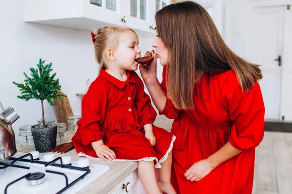 A mãe alimenta a filha de uma colher. Família na cozinha brilhante . — Fotografia de Stock