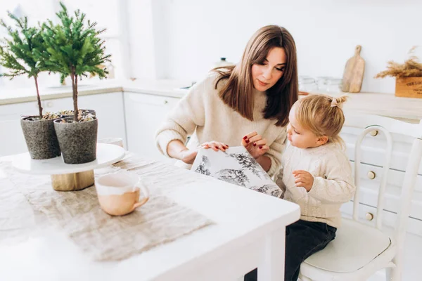 Mam voedt haar dochter met een lepel. Familie in de lichte keuken. — Stockfoto