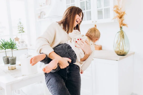 A mãe alimenta a filha de uma colher. Família na cozinha brilhante . — Fotografia de Stock