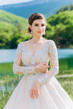 Gelin, yeşil çimlerin ve gölün arkasında beyaz bir gelinlik giyiyor..