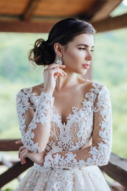 Gelin, yeşil çimlerin ve gölün arkasında beyaz bir gelinlik giyiyor..