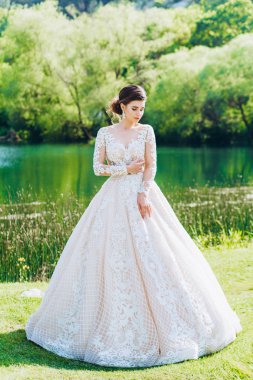 Gelin, yeşil çimlerin ve gölün arkasında beyaz bir gelinlik giyiyor..