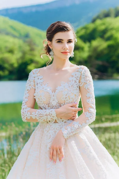 Gelin, yeşil çimlerin ve gölün arkasında beyaz bir gelinlik giyiyor..