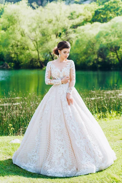 Gelin, yeşil çimlerin ve gölün arkasında beyaz bir gelinlik giyiyor..