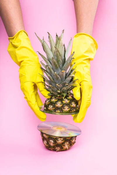 Sliced pineapple in hands in yellow gloves on a pink background. Minimalistic pineapple and abstraction with disks. — Stok fotoğraf