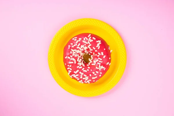 Pembe arka planda sarı bir tabakta pembe çörek. Şeker ve obezite. Soyutlama ve minimalizm. — Stok fotoğraf