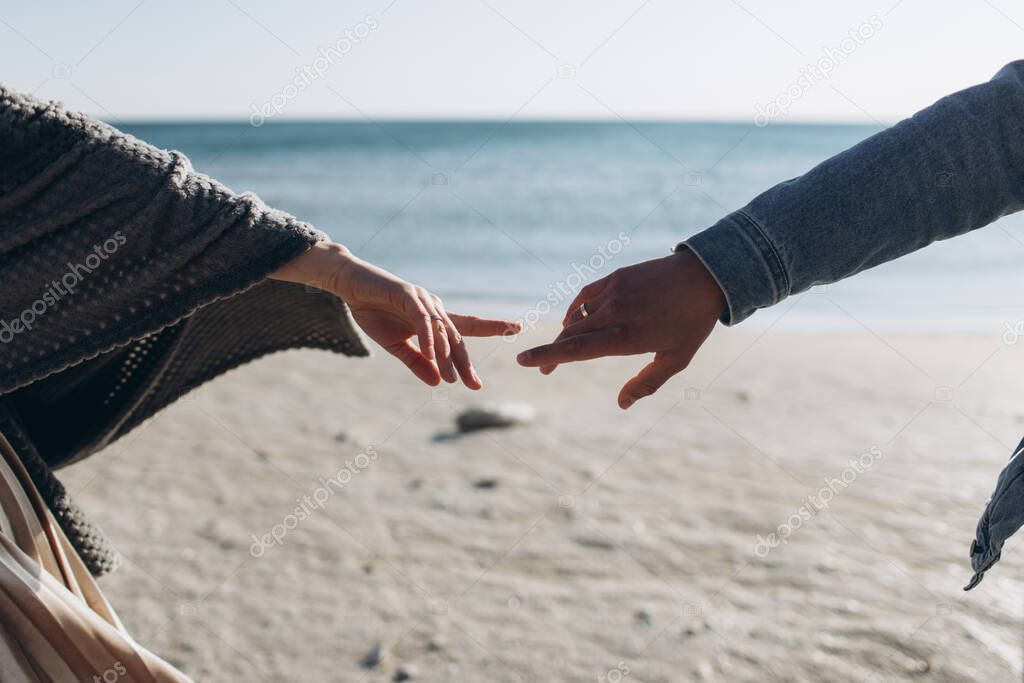 Hands of a couple against the background of the sea stretch to each other.