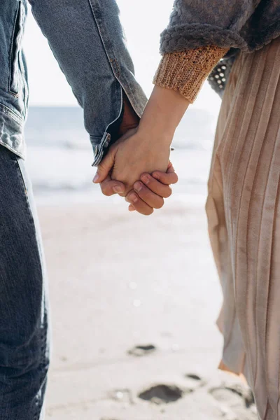 Bir çiftin elleri denizin arka planında birbirine uzanır..