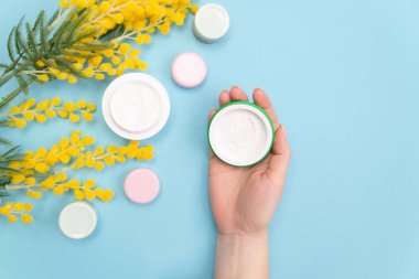 Mavi arka planda nemlendirici el kremi ve çiçekler. El bakımı. Ellerin kuru derisinden kurtulma. Boşluğu kopyala